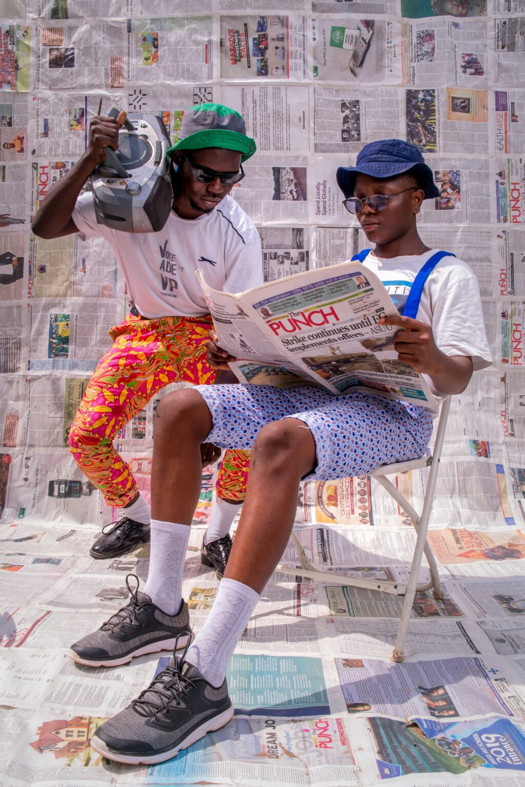 Two men sitting on a chair reading a newspaper.